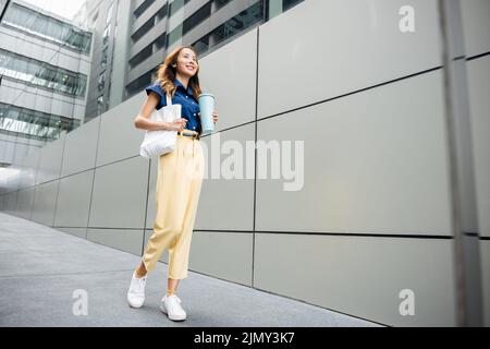 Asiatische schöne Geschäftsfrau zuversichtlich lächelnd mit Stofftasche hält Stahl Thermoskannen Becher Wasser Glas sie zu Fuß im Freien auf der Straße in der Nähe Modus Stockfoto