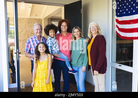 Porträt einer lächelnden Familie mehrerer Rassen, die durch die Flagge amerikas am Eingang steht Stockfoto