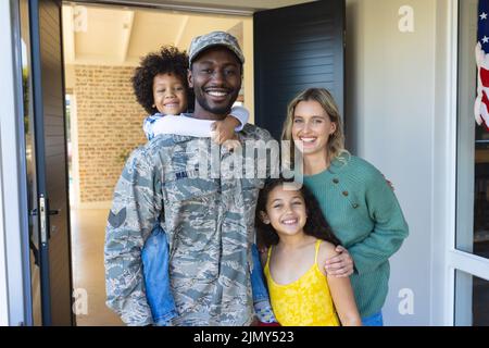 Porträt eines glücklichen multirassischen Soldaten mit Frau und Kindern, die am Eingang des Hauses stehen Stockfoto