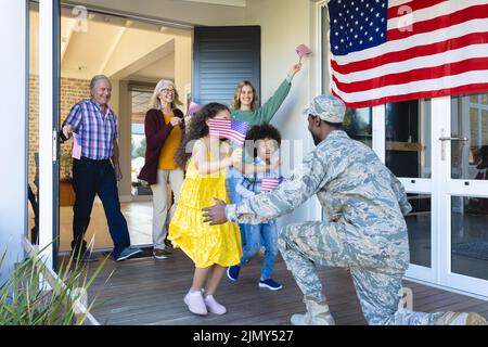 Multirassische Familie mit mehreren Generationen und Flagge amerikas, die Soldaten im Haus willkommen heißt Stockfoto