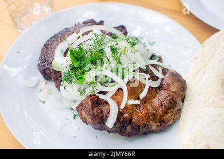 Appetitlich gegrilltes Schweinekotelett mit Zwiebeln und Dill auf dem weißen Teller. Saftiges Fleisch. Kebab. Stockfoto