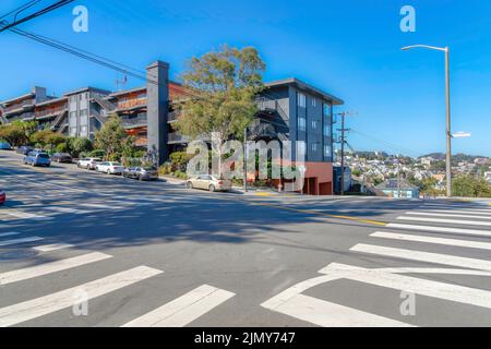 Apartmentgebäude an der Ecke in der Nähe der Kreuzung mit dem Fußgängerüberweg in San Francisco, CA. Apartmentgebäude auf der anderen Straßenseite mit zeitgenössischem Design Stockfoto