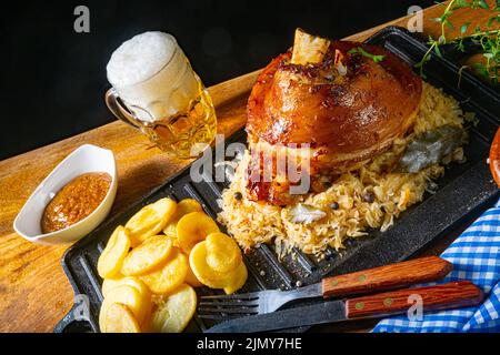 Rustikales Schweinshaxe mit Sauerkraut, süßem Senf und gebratenen Kartoffeln Stockfoto