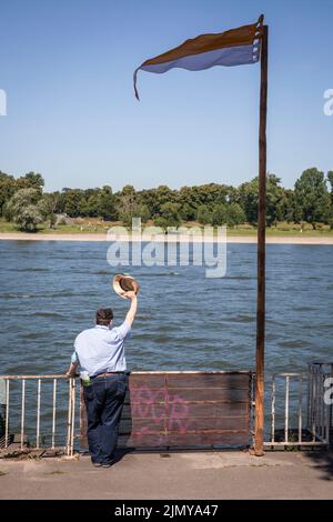 Mann, der am Rheinufer im Mülheimer Bezirk steht und mit dem Hut winkt, Köln, Deutschland. Mann steht am Rheinufer im Stadtteil Mülheim und w Stockfoto