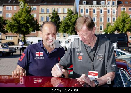 Kiel, Deutschland. 08. August 2022. Walter Röhrl (r) unterschreibt vor Beginn der Wiederbelebung der Olympischen Rallye 1972 ein Autogramm auf dem Fahrzeug des Teilnehmers Franz Vieghofer aus Österreich. 197 Teams mit Fahrzeugen von 44 verschiedenen Automarken, die zwischen 1950 und 1990 gebaut wurden, werden in sechs Etappen nach München kommen. Quelle: Frank Molter/dpa/Alamy Live News Stockfoto