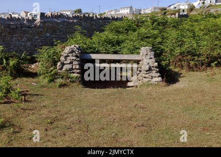 Material aus lokalem Material, das eine lange, robuste Bank bildet, die sich im Schutz einer großen Trockensteinmauer befindet und einen Blick auf den Kanal von Bristol bietet. Stockfoto