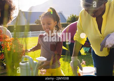 Multirassisches lächelndes Mädchen mit Mutter und Großmutter, die während eines sonnigen Tages im Hof Pflanzen Stockfoto