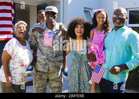 Porträt eines glücklichen mehrrassischen Soldaten der Armee mit einer mehrgenerationenigen Familie, die vor dem Haus steht Stockfoto