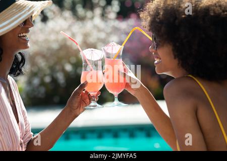 Frauen aus der Biracial Millennial-Gruppe lachen und toasten Cocktails, während sie im Sommer eine Poolparty genießen Stockfoto