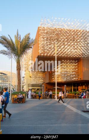 VAE, Dubai - 30. November 2021: EXPO 2020. Die Menschen gehen auf Wegen zwischen Pavillons. Ausstellungshalle Polen in Abendstrahlen des Sonnenuntergangs. Stockfoto