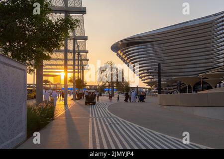 VAE, Dubai - 30. November 2021: Ausstellung EXPO 2020. Menschen gehen zwischen Pavillons entlang. Ausstellungshalle Mobilität in den Abendstrahlen des Sonnenuntergangs. Stockfoto