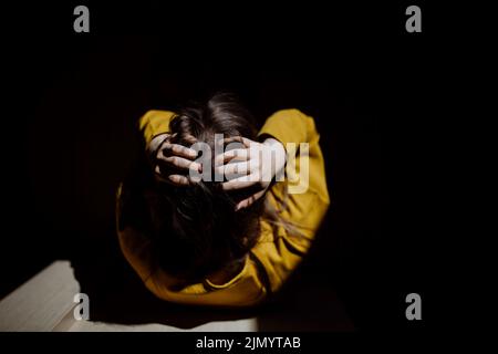 Draufsicht auf eine nicht erkennbare Frau, die an Depressionen leidet und zu Hause weint und den Kopf in den Händen hält. Stockfoto