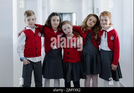 Fröhliches Schulkind mit Down-Syndrom, das mit ihren Klassenkameraden im Schulkorridor steht und die Kamera anschaut. Stockfoto