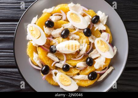 Remojon Andaluz enthält frische Orangen, Zwiebel, gekochte Eier, schwarze Oliven und köstlichen Salz-Kabeljau aus nächster Nähe auf einem Teller auf dem Tisch. Horizontale Ansicht von oben Stockfoto