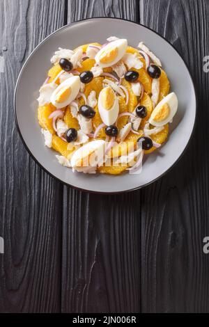 Remojon granadino, Salz-Kabeljau-Orangen- und Olivensalat, spanische Küche aus nächster Nähe auf einem Teller auf dem Tisch. Vertikale Draufsicht von oben Stockfoto