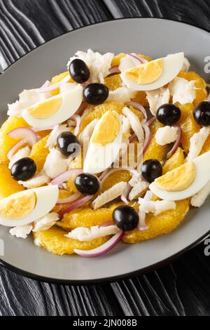 Spanische Küche Remojon-Kabeljau, Ei, Oliven-, Zwiebel- und Orangensalat in Nahaufnahme auf einem Teller auf dem Tisch. Vertikal Stockfoto