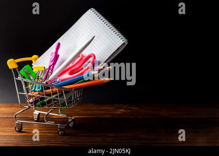 Einkaufswagen mit Schreibwaren oder Büromaterial auf dunklem Hintergrund. Stockfoto