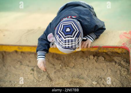 Kind im Sandkasten. Vorschulkinder auf dem Spielplatz. Kleiner Junge gräbt Boden. Stockfoto