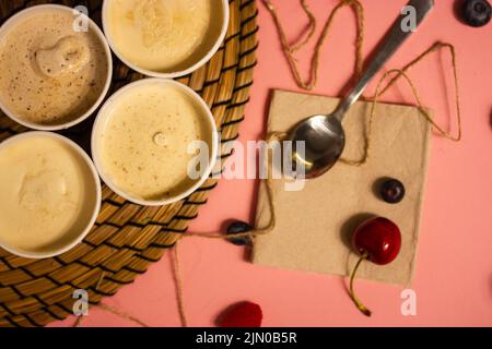 Auf dem Tisch steht eine Auswahl aus vier Dosen italienischem Eiseis, rote Kirschen auf einer rosa Tischdecke verstreut, Dessertlöffel. Ein köstliches, c Stockfoto