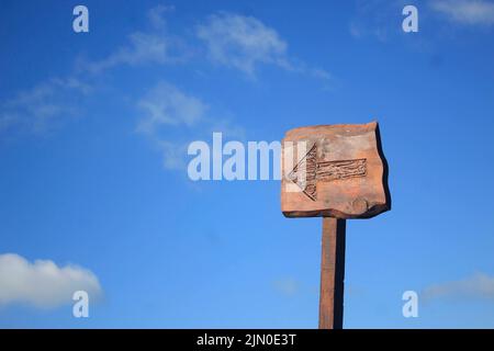 Nahaufnahme eines Pfeilzeichens, das links auf einem Holzpfosten gegen einen blauen Himmel zeigt - Richtungskonzept Stockfoto