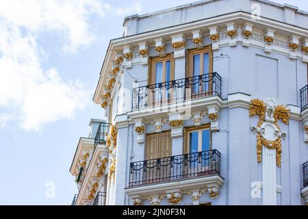 Madrid, Spanien. Juni 1 2022. Ecke eines schönen historischen Wohngebäudes mit einer wunderschön dekorierten grau-blauen Fassade, Fenstern mit Holzschinkensaumglas Stockfoto