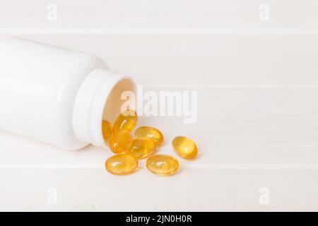 Omega-3 Kapseln liegen in einer weißen Flasche auf einem Tischhintergrund. Fischöl Tabletten Draufsicht. Biologisch aktive Zusatzstoffe. omega 6, Omega 9, Vitamin A, E, Stockfoto