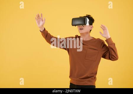 Junger Mann in braunem Sweatshirt, der Videospiel im VR-Headset spielt Stockfoto