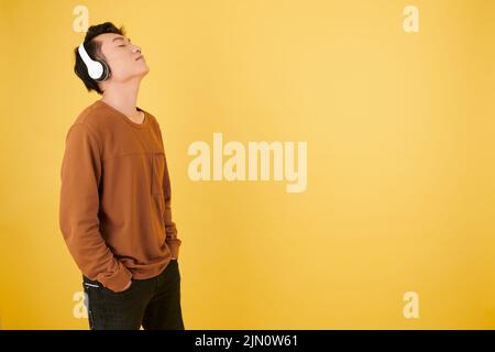 Der junge Mann lehnte sich den Kopf zurück, als er sein Lieblingslied über Kopfhörer genießen konnte Stockfoto