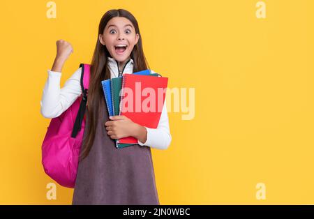 Erfolgreiches Kind mit Schulrucksack und Arbeitsbuch auf gelbem Hintergrund Stockfoto