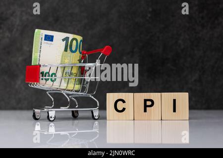 Bargeld rollt in einem Einkaufswagen, Euro-Banknoten mit Holzblöcken und Wort CPI auf weißem Tisch auf dunkelgrauem Hintergrund. Verbraucherpreisindex, Verbraucherpreis ind Stockfoto