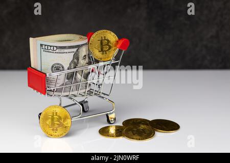 Bitcoin und Dollarrolle im Warenkorb oder Warenkorb auf dunkelgrauem Hintergrund. Kaufen oder verkaufen. Das Konzept des Einflusses der virtuellen Währung auf die econ Stockfoto