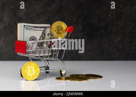 Bitcoin und Dollarrolle im Warenkorb oder Warenkorb auf dunkelgrauem Hintergrund. Kaufen oder verkaufen. Das Konzept des Einflusses der virtuellen Währung auf die econ Stockfoto