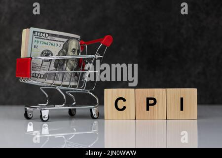 Dollarrolle im Einkaufswagen und Holzblöcke mit dem Wort cpi auf dunkelgrauem Hintergrund. Kaufen oder verkaufen. Geschäfts- und Verbraucherpreisindex Konz Stockfoto