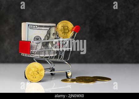 Bitcoin und Dollarrolle im Warenkorb oder Warenkorb auf dunkelgrauem Hintergrund. Kaufen oder verkaufen. Das Konzept des Einflusses der virtuellen Währung auf die econ Stockfoto