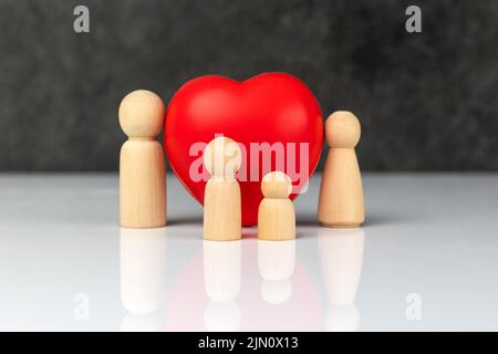 Vier kleine Holzfiguren, die eine Familie symbolisieren - eine Mutter, ein Vater und zwei Kinder, in der Nähe eines großen roten Herzens. Das Konzept der Liebe und Fürsorge der Familie. Stockfoto