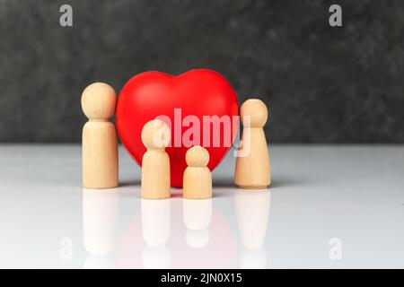 Vier kleine Holzfiguren, die eine Familie symbolisieren - eine Mutter, ein Vater und zwei Kinder, in der Nähe eines großen roten Herzens. Das Konzept der Liebe und Fürsorge der Familie. Stockfoto