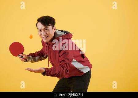 Lächelnder junger asiatischer Mann, der Tischtennis spielt, isoliert auf Gelb Stockfoto