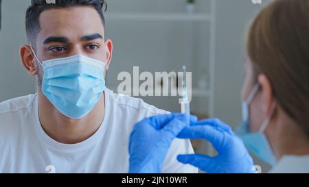 Blick von hinten Frau Arzt Krankenschwester hält Spritze mit Medikamenten-Impfstoff für covid männlichen Patienten hispanic arabischen Mann in Maske Wellen Hände keine weigert Stockfoto