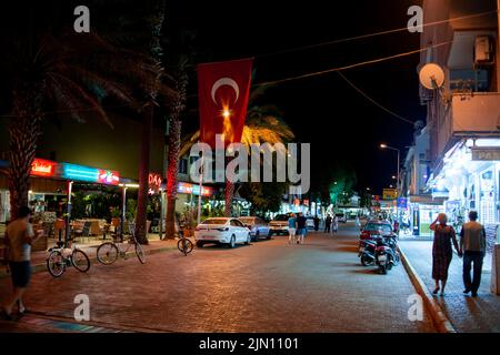 Touristen kommen abends an einer Cafeteria und einem Souvenirladen in einem kleinen Ferienort vorbei. Street Food und Souvenirläden an der Hauptstraße in der Nacht. Turunc, Tur Stockfoto