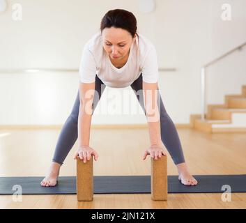 Eine Schwangerin ist im Yoga engagiert. Stehend halb nach vorne Biegung oder Ardha Uttanasana mit Blöcken Stockfoto