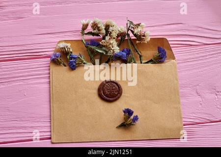 Beigefarbener Umschlag mit Blumen auf rosafarbenem Holzschreibtisch. Angebrachte braune Dichtung. Stockfoto