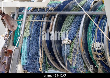 In einem holländischen Hafen rollte man blaue und grüne Fischernetze auf einem Heck eines Fischerbootes auf Stockfoto