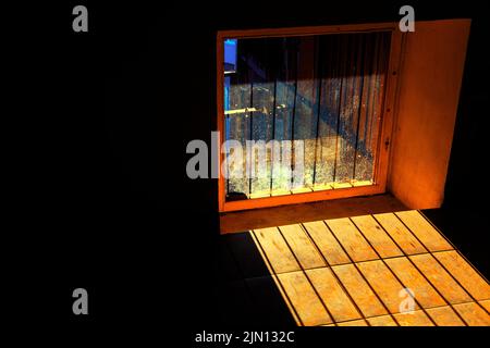 Gefängnisfenster mit Gitterrost. Fenster mit schmutzigem Glas. Sonnenlicht im dunklen Raum Stockfoto