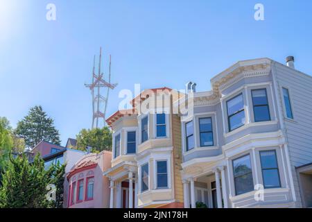 Blick auf Wildhäuser und den Sutro Tower von unten in San Francisco, CA. Es gibt zwei Häuser auf der rechten Seite mit Erkerfenstern und dekorativen Veranda Säulen nea Stockfoto