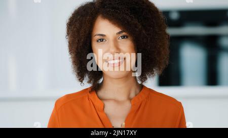 Lächelndes afroamerikanisches Mädchen mit lockigen Haaren, die Geschenk zeigen, Geschenkschachtel in rotes Papier mit goldenem Band verpackt, wünscht alles gute zum Geburtstag Stockfoto