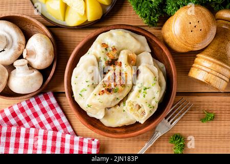 Pierogi-, Vareniky- oder Kartoffelknödel in Tonschüssel auf Holztisch-Hintergrund, Draufsicht. Traditionelle ukrainische Küche Essen Stockfoto