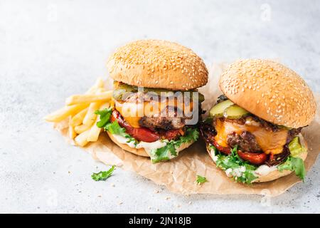 Cheeseburger mit gegrilltem rotem Paprika, Rucola und Dill-Gurken auf Pergamentpapier serviert. Grauer Steintropfen Stockfoto