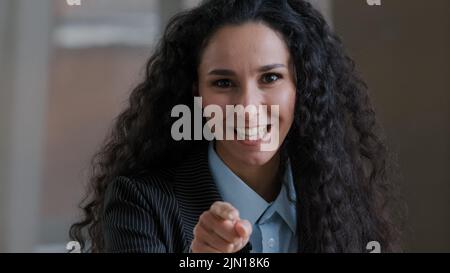 Arabisch lächelnde lockige Frau Angestellte Geschäftsfrau zeigt Zeigefinger auf Kamera emotional sprechend erklärt Corporate Items hey Sie Geste Stockfoto