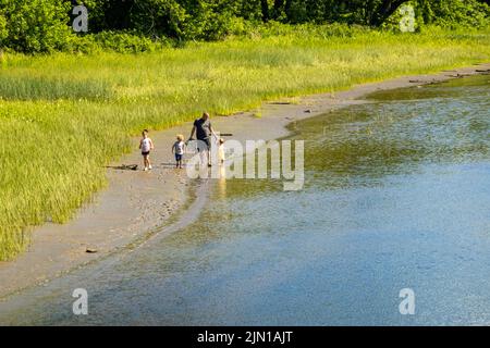 Vater und Kinder, die am Flussrand des Kennebec-Flusses in Hallowell Maine spazieren Stockfoto