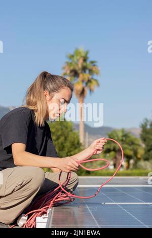 Vertikale Ansicht einer jungen Ingenieurin, die auf dem Dach eine Photovoltaik-Solaranlage installiert, alternative Ökoenergie-Konzept. Stockfoto